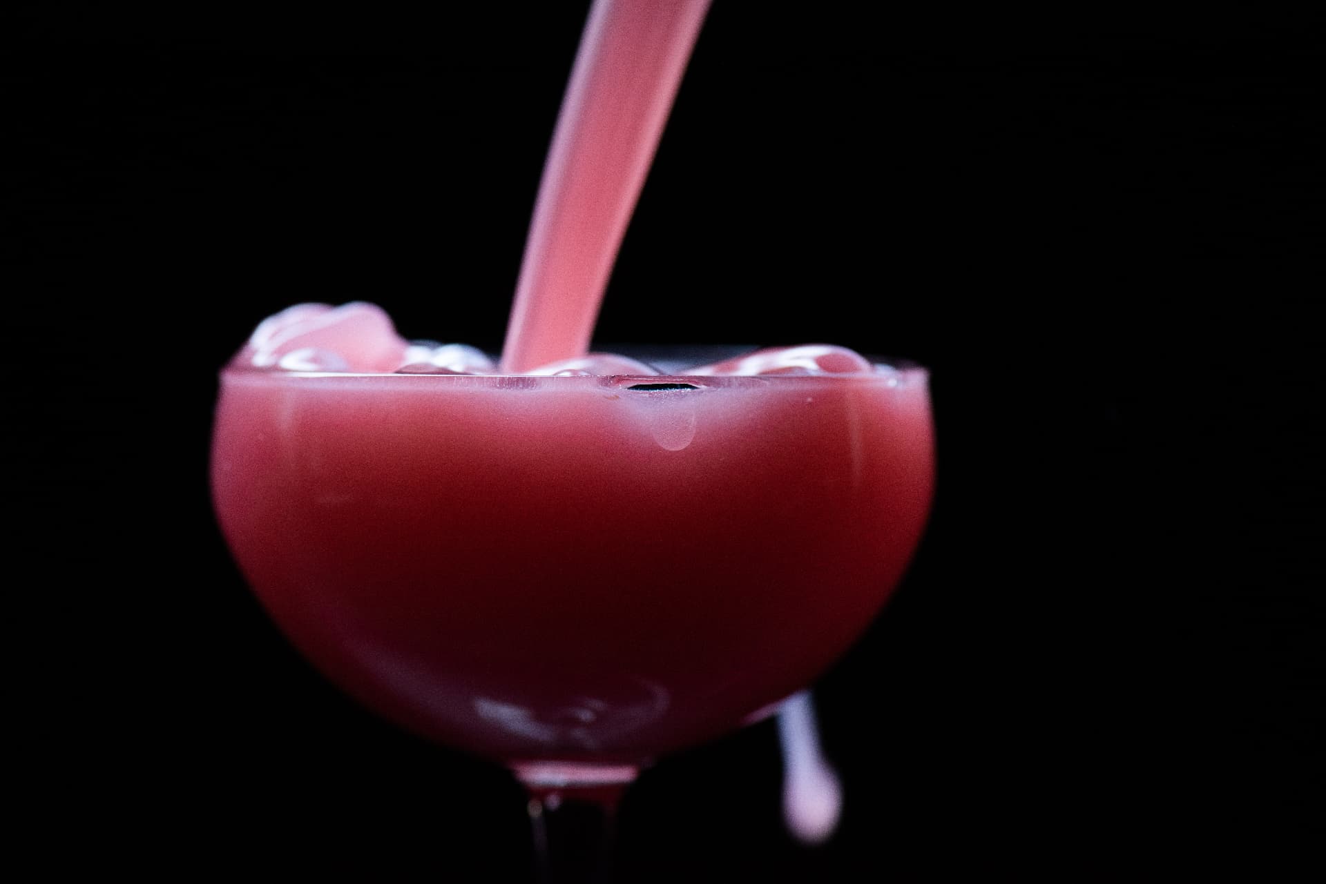 Pink cocktail being poured into a coupe glass