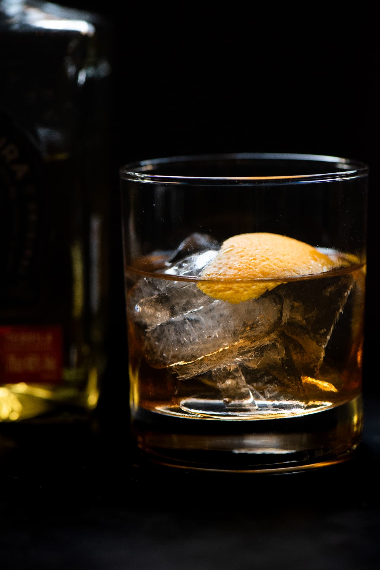 Old fashioned cocktail over a large ice cube with orange peel