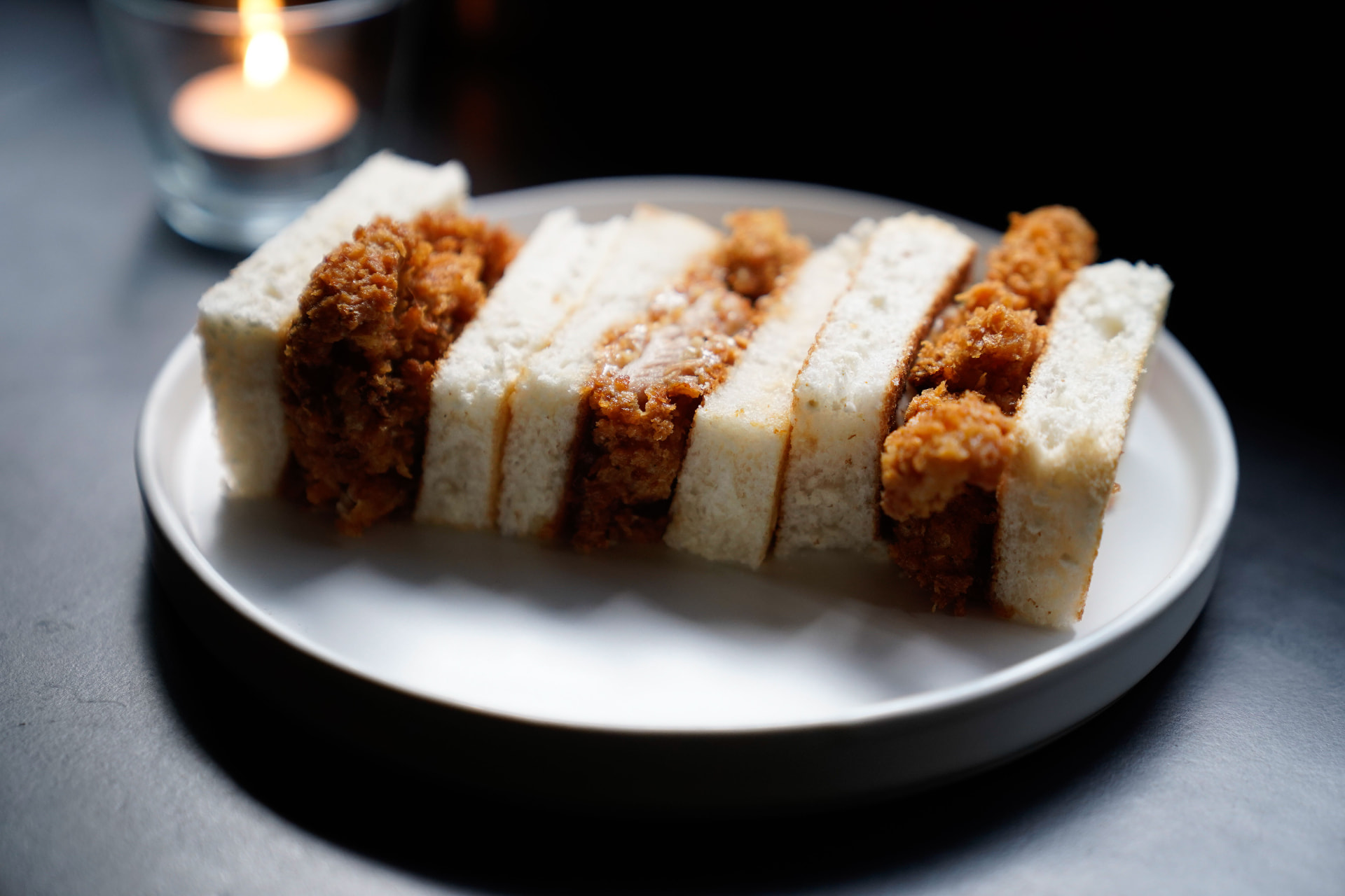 Sliced katsu sando on a white plate by candlelight